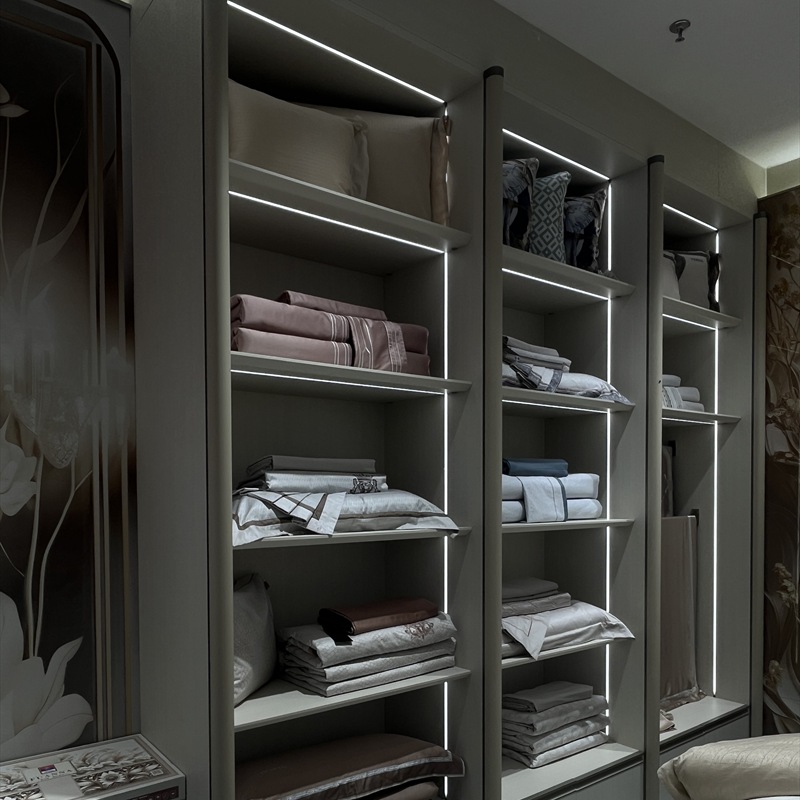 Angled view of illuminated shelves displaying pillows and folded bedding